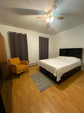 Un dormitorio con cama, ventilador de techo, una silla y cortinas.