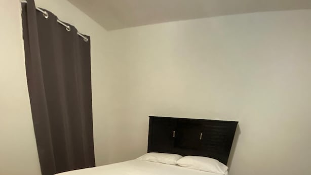 Ein ordentlich bezogenes Bett mit dunklem Kopfteil in einem Zimmer mit Holzböden und einem Streifenmuster-Teppich.