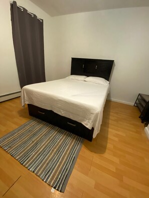 Una cama bien hecha con un cabecero oscuro en una habitación con piso de madera y un tapete a rayas.