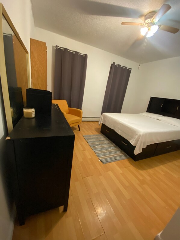 Un dormitorio con una cama, un escritorio, una silla, un ventilador de techo y una ventana con cortinas.