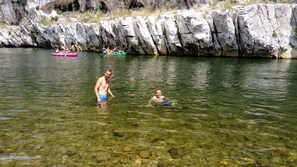 Um rio com águas cristalinas, margens rochosas e pessoas praticando caiaque.