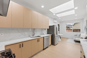 Cozinha moderna com bancada de mármore, eletrodomésticos de aço inoxidável e área de refeições com mesa branca e sofá.