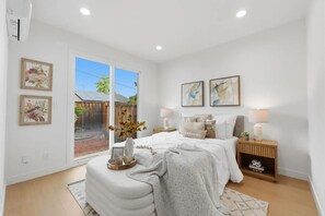A bedroom with a bed, bedside tables, a nightstand, a window, and artwork on the walls.