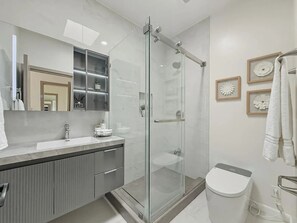 A modern bathroom with a glass-enclosed shower, a vanity with a sink, and a toilet.