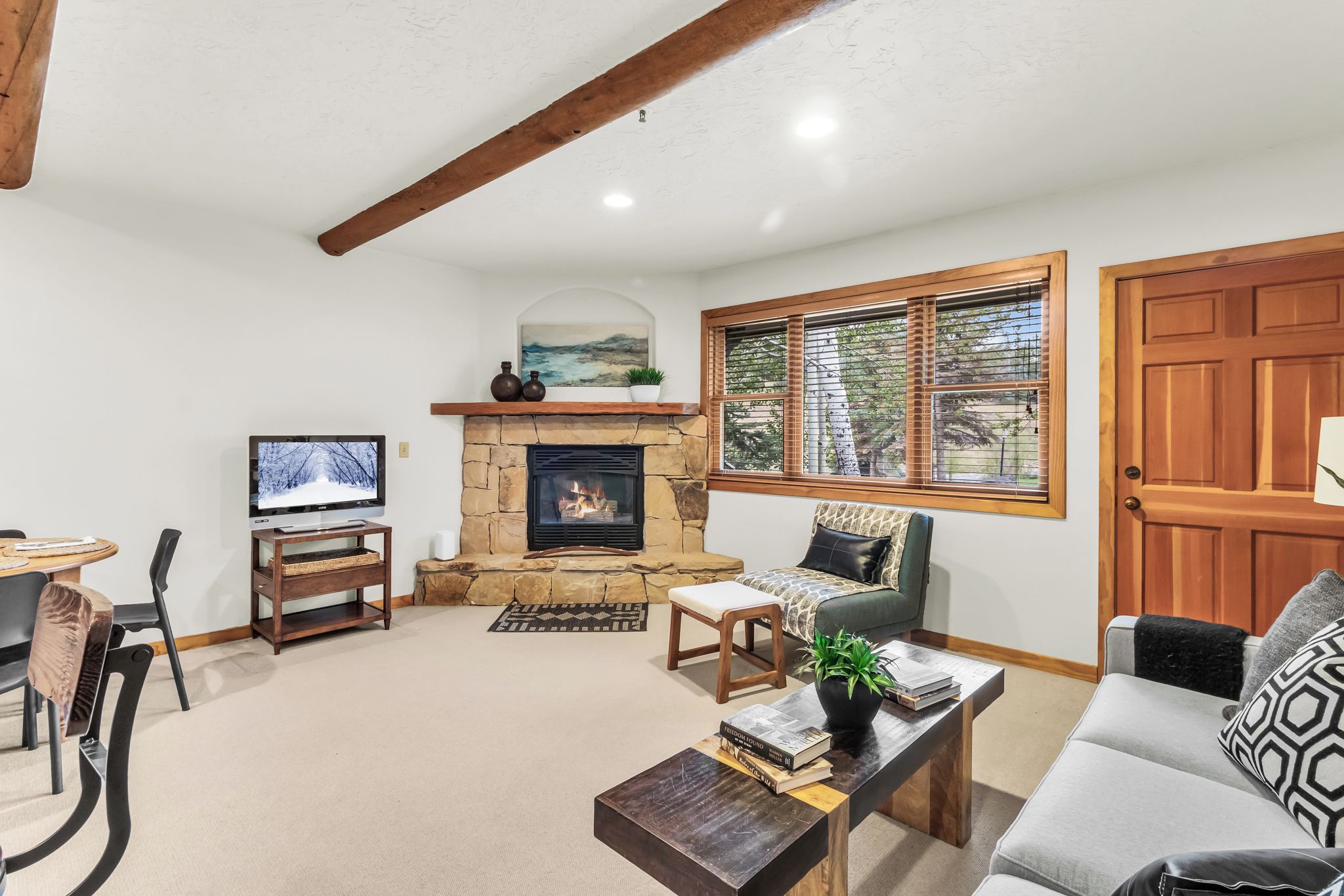 A living room with a stone fireplace, a television, a sofa, and a dining area with chairs.