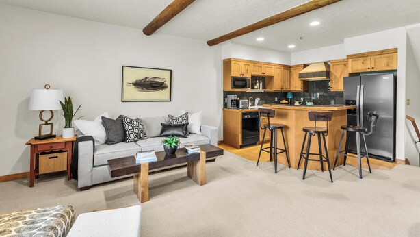 Ein modernes Wohnzimmer mit einer Couch, einem Couchtisch und einer Küchenzeile mit Holzschränken und einem Kühlschrank.