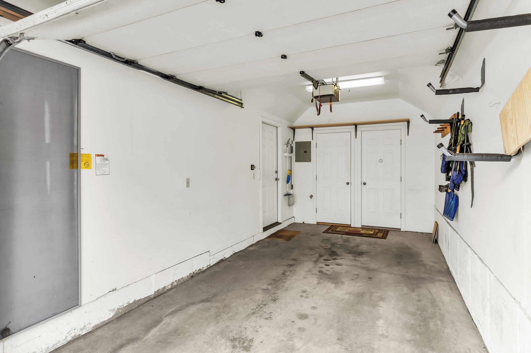 A clean, well-lit garage with white walls, a concrete floor, and a ceiling fan. There are two white doors, one with a metal handle and the other with a round doorknob.