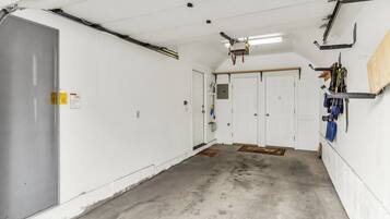 A clean, well-lit garage with white walls, a concrete floor, and a ceiling fan. There are two white doors, one with a metal handle and the other with a round doorknob.