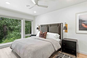Een moderne slaapkamer met een groot bed, een plafondventilator en uitzicht op groen.