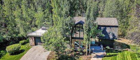A two-story house with a stone foundation, a covered patio, and a driveway leading to a garage.