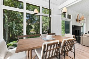 Een ruime eetruimte met een houten tafel en stoelen, grote ramen en uitzicht op groen.