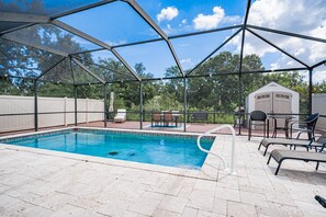Piscina exterior techada con zona de patio, mobiliario y un cobertizo al fondo.