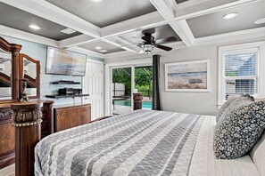 Ein Schlafzimmer mit Bett, Deckenventilator, Fernseher und Fenster mit Blick auf einen Swimmingpool.