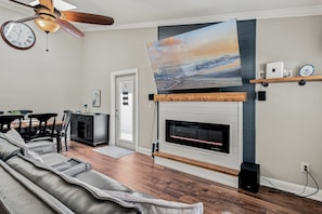 Una sala de estar con chimenea, ventilador de techo y comedor con mesa y sillas.