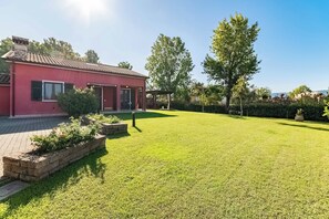 A red building with a tiled roof, a well-maintained lawn, and a pergola structure. - Villa con piscina privata tra natura e 5 terre. (Sarzana)