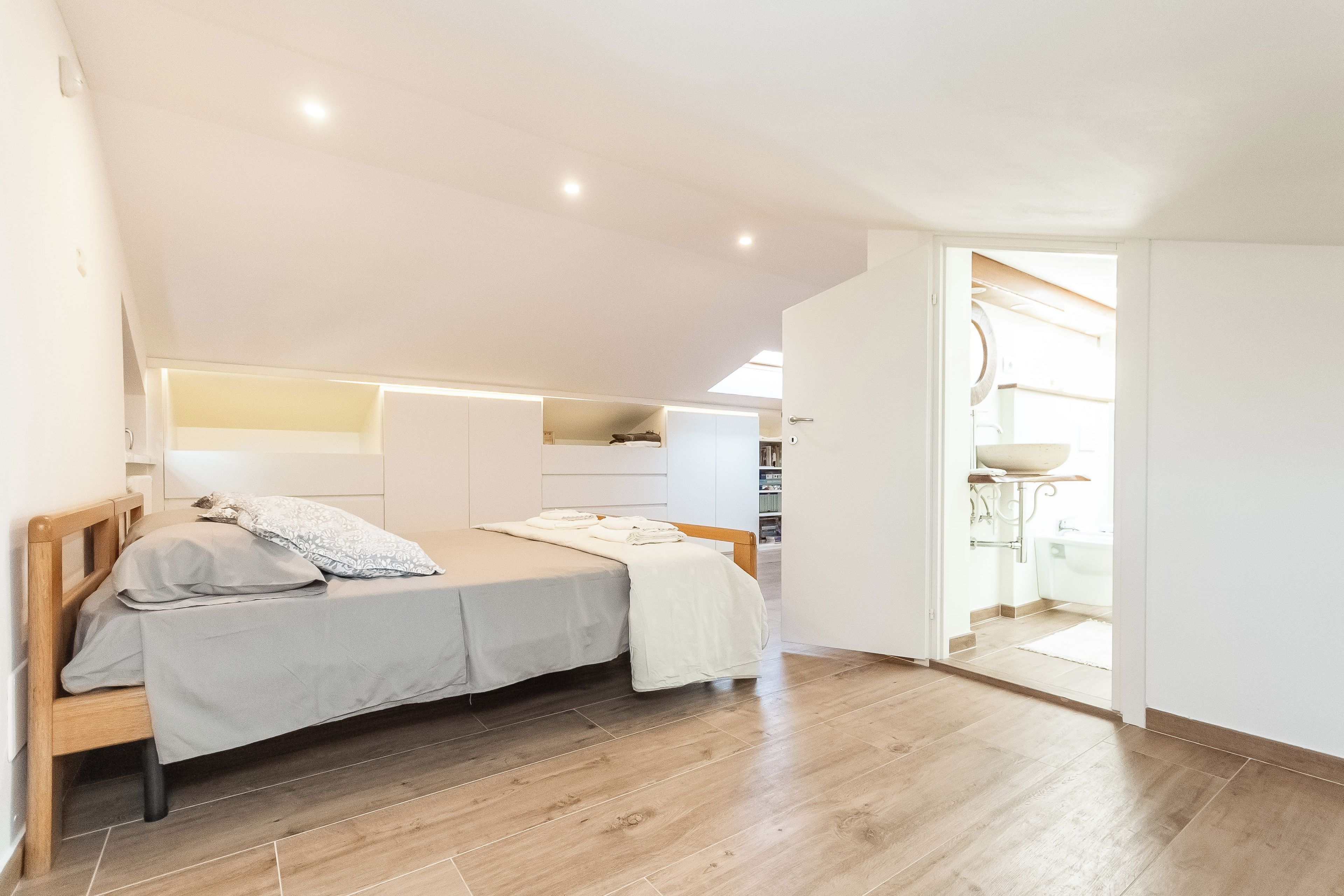 A bedroom with a bed, bedside tables, a wardrobe, and a bathroom visible through an open door.