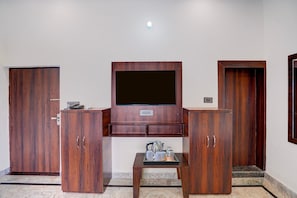 A room with a television mounted on a wooden cabinet, two wooden doors, a small table with a kettle and cups, and a light fixture on the ceiling. - Deluxe With Twin Bed Ummed Palace (Mathura)