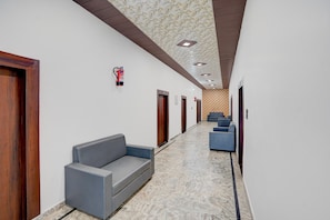 A hallway with a marble floor, a grey sofa, and blue chairs. - Deluxe With Twin Bed Ummed Palace (Mathura)