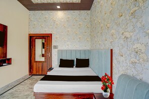 A bedroom with a bed, a wooden door, a mirror, a bedside table, and a red flower vase. - Deluxe With Twin Bed Ummed Palace (Mathura)