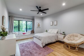 A bedroom with a bed, bedside tables, a chair, a window with curtains, a ceiling fan, and a view of greenery outside. - Beautiful spacious 5 bedroom on half an acre, with pool and tons of amenities. (Dallas)