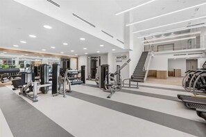 Ein moderner Fitnessraum mit verschiedenen Trainingsgeräten, einer Trinkstation und einer Treppe, die in einen oberen Bereich führt.