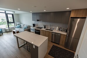 A modern kitchen with a central island, built-in appliances, and a view through the window. - Luxury condo with so many amenities! (Kelowna)
