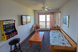 A room with a bed, a table, a chair, a ceiling fan, a television, and a Pac-Man arcade game. - 7522 - Island Thunder (Avon)