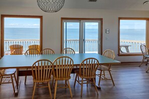 A dining area with a large table and chairs, large windows with a view of the sea, and a ceiling light fixture. - 7522 - Island Thunder (Avon)