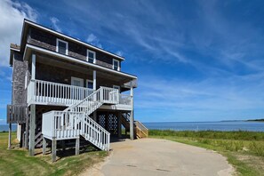 A two-story beachfront property with a wooden deck and a staircase leading to a balcony. - 7522 - Island Thunder (Avon)