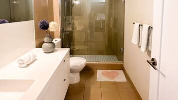 A modern bathroom with a glass-enclosed shower, a white sink, and a toilet.