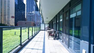 A balcony with a view of a cityscape, a table with chairs, and a grassy area.