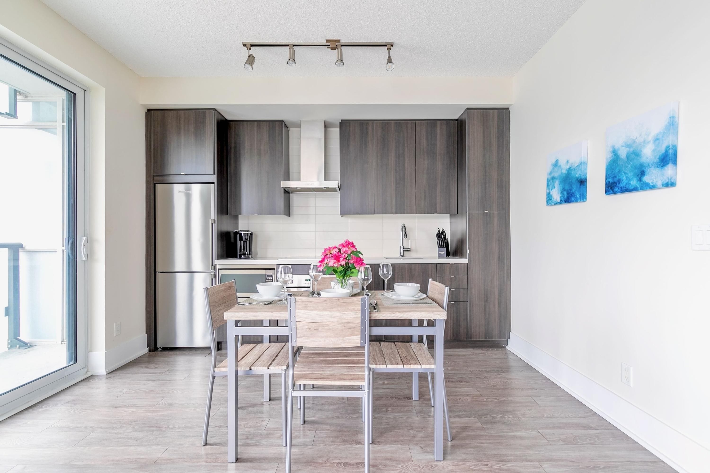 A modern kitchen with dark cabinets, a stainless steel refrigerator, and a dining area with a wooden table and chairs.