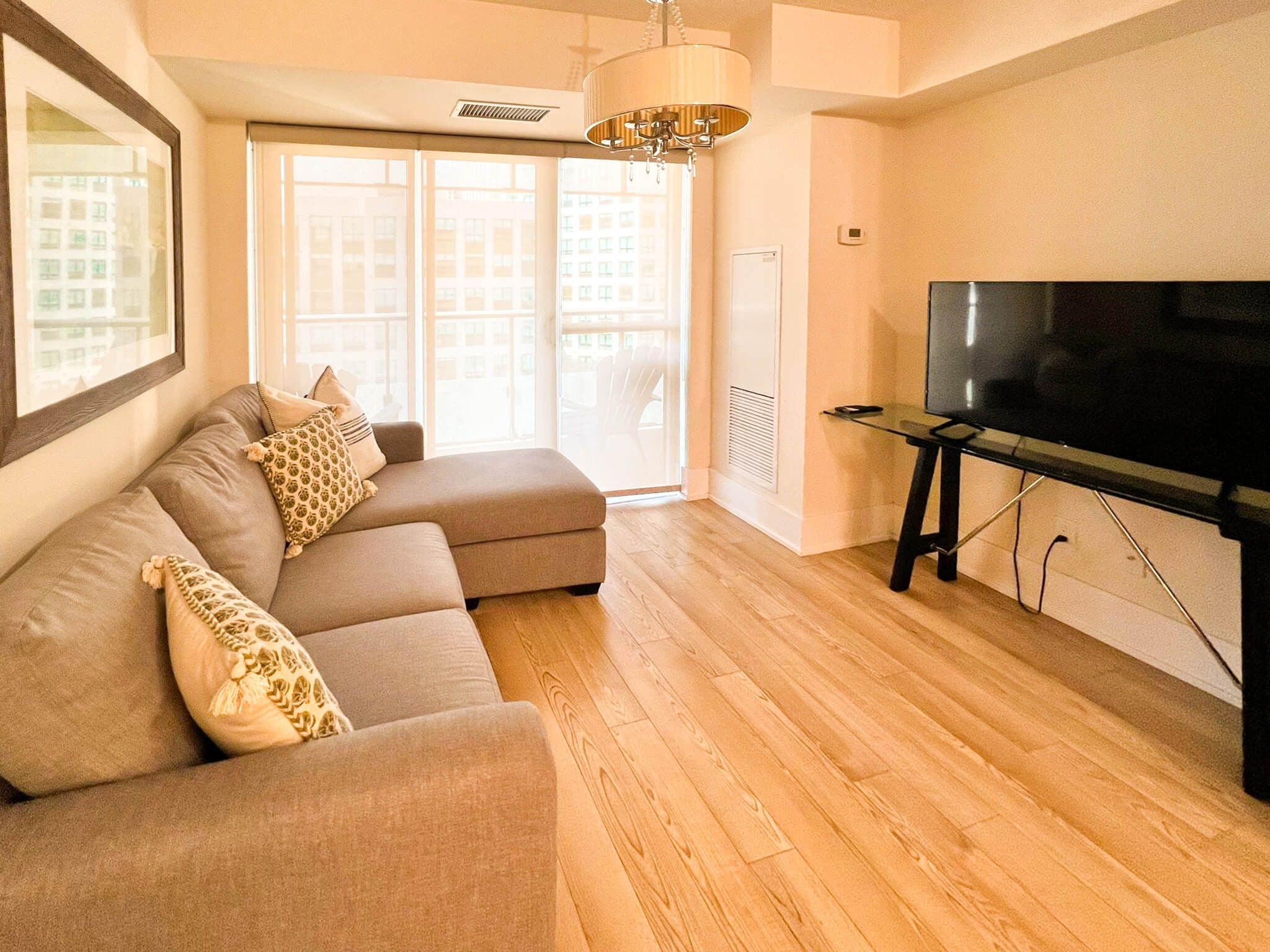A living room with a sectional sofa, a flat-screen TV on a stand, and a large window with a view of buildings.