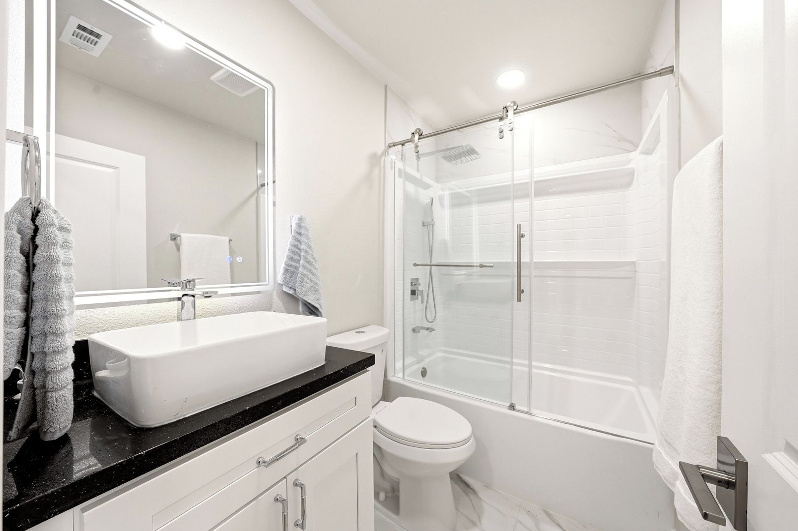 A modern bathroom with a large mirror, a white sink, a toilet, and a glass-enclosed shower.