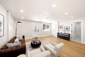 Un salon spacieux avec un canapé en cuir marron, une table basse ronde et un fauteuil blanc. On y trouve une console noire ornée d’objets décoratifs et une porte blanche avec un panneau en verre.