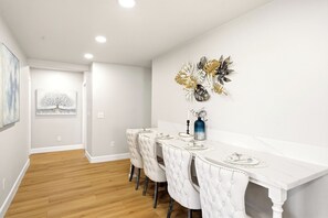 Un espace repas comprenant une table en marbre blanc, des chaises à revêtement blanc et un élément décoratif fixé au mur.