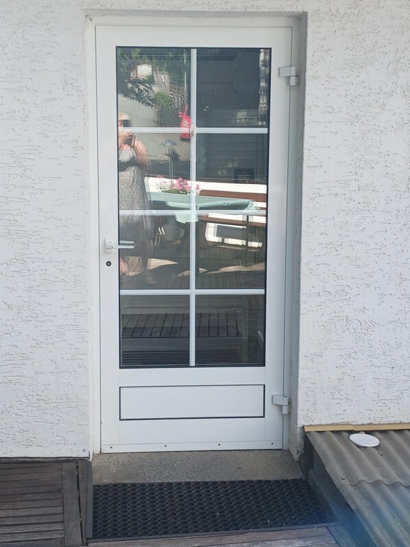 Une porte blanche avec un panneau de verre, une petite marche menant à l’entrée et une plaque de protection en métal au bas de la porte.