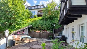 A wooden deck with outdoor furniture, surrounded by lush greenery and a wooden fence. - Vrbo Property (Winterberg/Züschen)