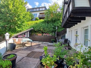 Une terrasse en bois, agréée de mobilier d’extérieur, entourée d’une végétation luxuriante et d’une clôture en bois.