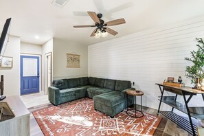 Uma sala de estar moderna com sofá seccional, uma mesinha lateral, um tapete decorativo e um ventilador de teto.