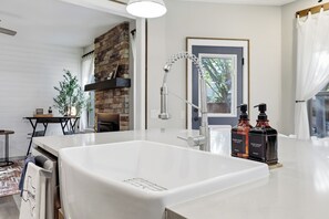 A modern bathroom with a large white bathtub, a stone accent wall, and a window with blinds. - Family Friendly Retreat, Fire Pit, Games, More (McKinney)