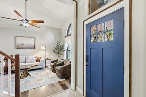 Un salon avec une porte bleue, un ventilateur de plafond, un canapé, une table basse et un tapis.