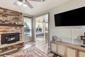 A living room with a fireplace, a flat-screen TV mounted on the wall, and a view into the adjacent dining area. - Family Friendly Retreat, Fire Pit, Games, More (McKinney)