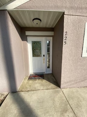 Una entrada de casa con una puerta blanca, un pequeño porche y el número '225' en la pared.