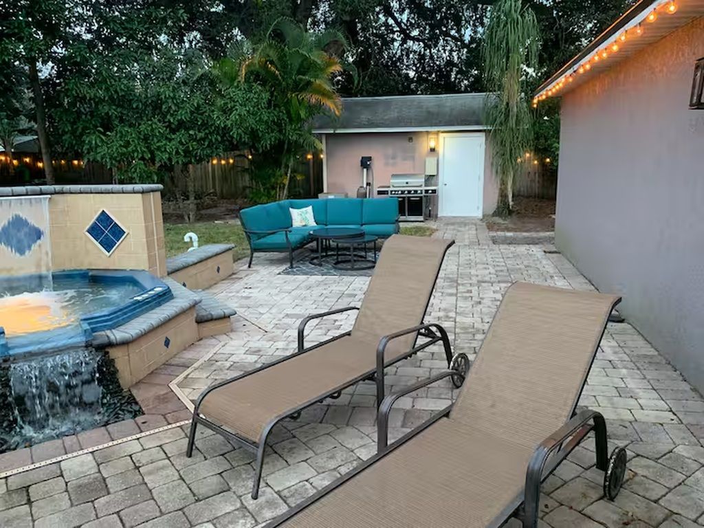 Een terras buiten met lounge fauteuils, een jacuzzi en een barbecueplek.