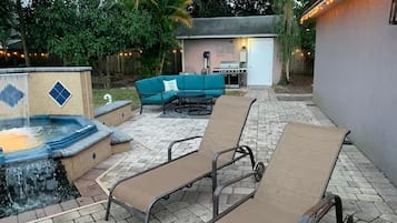 Um pátio externo com cadeiras de descanso, uma banheira de hidromassagem e espaço para churrasco.