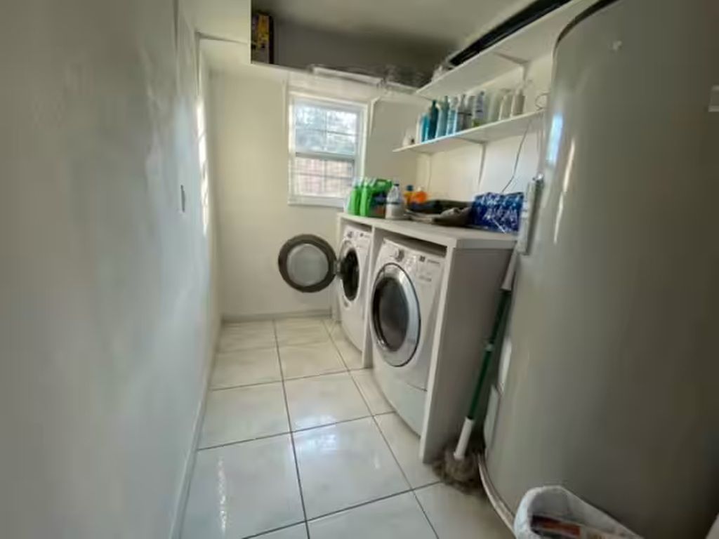 Een wasserette met een wasmachine, droger en planken met schoonmaakmiddelen.