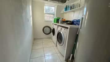 Een wasserette met een wasmachine, droger en planken met schoonmaakmiddelen.