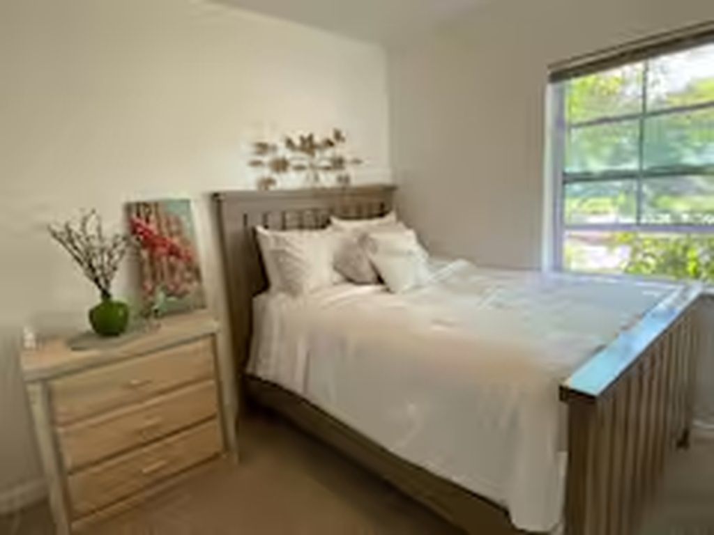 Een slaapkamer met een bed, nachtkastje, dressoir en een raam.