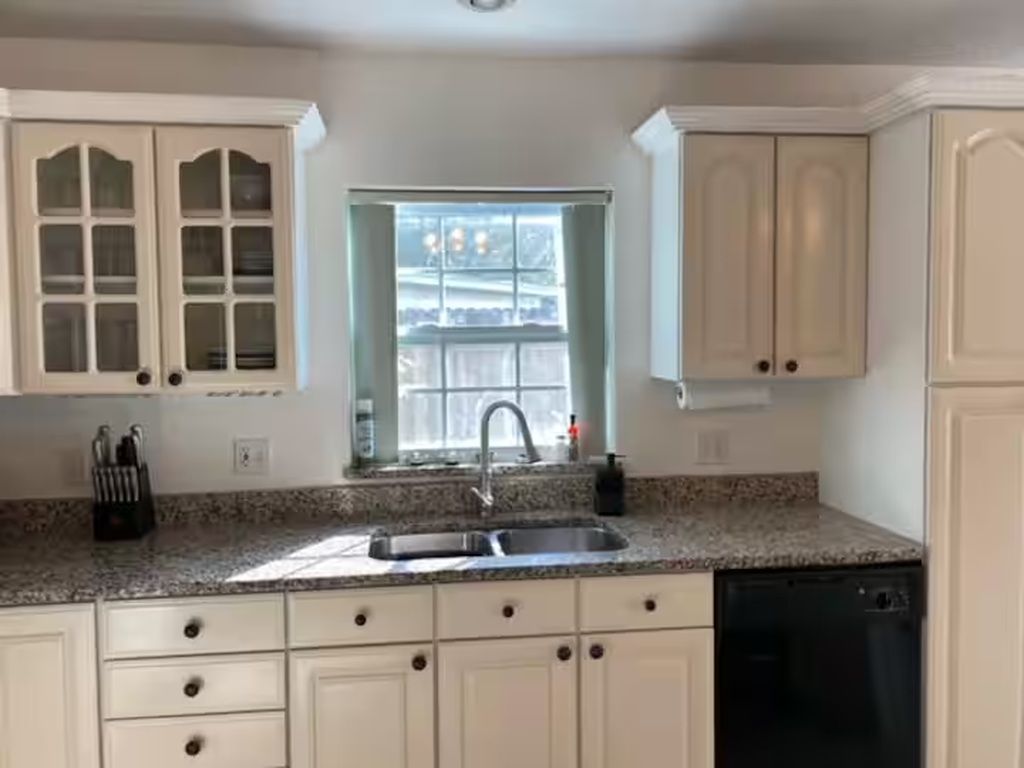 Cozinha com armários brancos, bancada de granito, pia dupla e janela com vista.